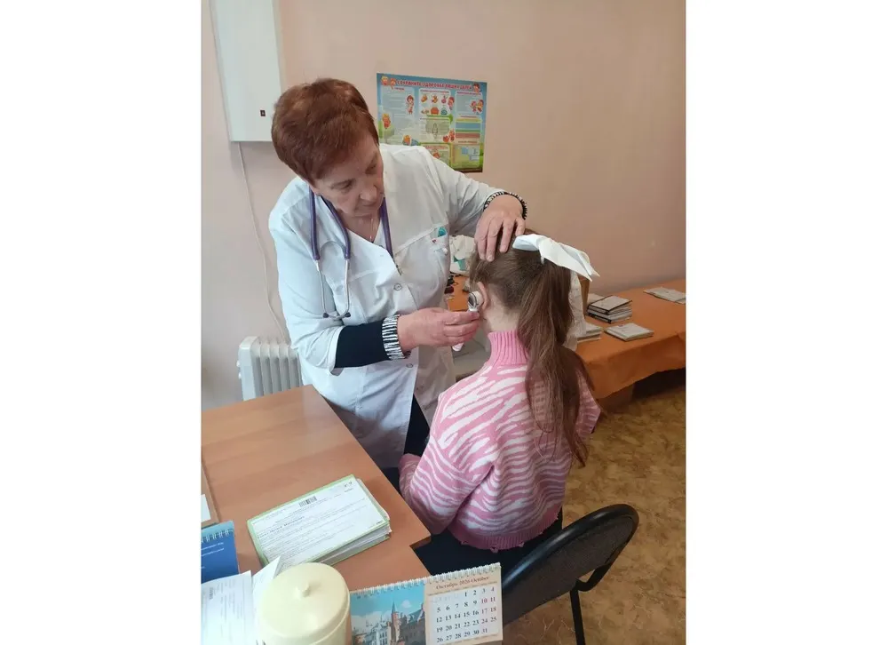 Педиатр проводит осмотр уха ребенка отоскопом