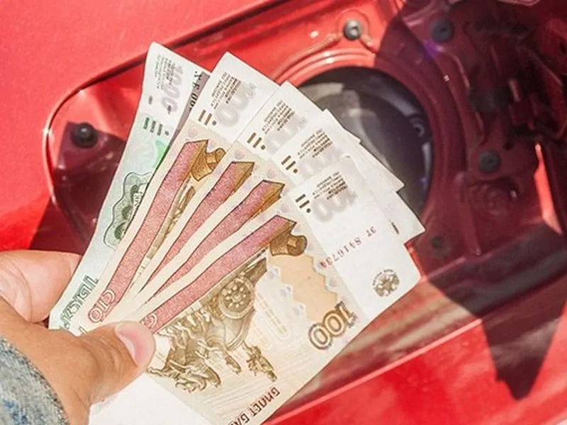Деньги в руке у люка бензобака автомобиля