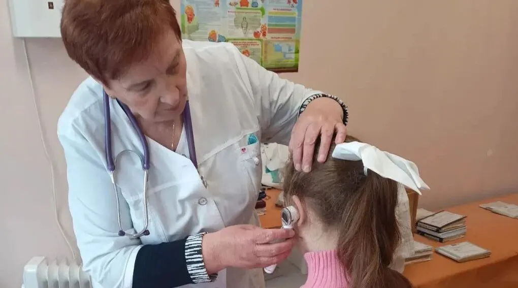 Педиатр проводит осмотр уха ребёнка отоскопом